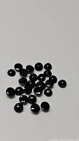 Multiple small round polished jet black onyx cabochon gemstones scattered on a white background, showing smooth domed surfaces and glossy finish.