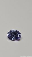Close-up image of a natural light purple oval cut tanzanite with visible facets and clarity under white lighting.