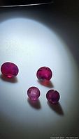 Four natural oval sapphires in red, pink, and dark blue tones placed on a light surface under direct light showing color and internal inclusions.