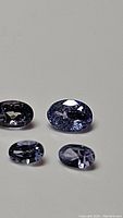 Four natural oval cut tanzanite gemstones displayed on a plain background, showing color and cut quality.