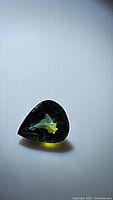 Close-up photo of the natural tri-colored sapphire showing green, yellow, and blue hues in a polished gemstone shape.
