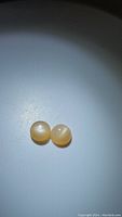 Two round peach moonstones side by side on a plain surface, showing their smooth cabochon shape and translucent peach color under neutral lighting.