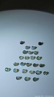View of 27 natural alexandrite cabochon gemstones under natural white light showing green to yellow hues.