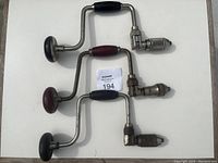 Three vintage Stanley hand drills laid flat showing overall shape and wooden handles, metal crank shafts, and drill chucks.