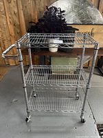 Front view of metal trolley bar server cart showing three wire shelves and tubular handle with wheels.