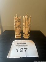 Two ivory-colored miniature Asian warrior figurines standing on a shelf with lot tag 197 in front.