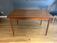 Front view of closed table showing rectangular teak top and tapered legs.