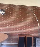 Full view of lamp showing extended stainless steel arch and dome shade against brick wall
