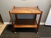 Front view of teak bar cart showing two tiers and casters