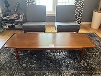 Front view of the walnut coffee table on patterned rug between two chairs.
