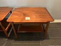Full view of one walnut end side table with scalloped edges and lower shelf.