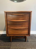 Front view of walnut nightstand with three drawers and curved handles.