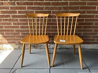 Pair of Mid century modern Danish spindle back chairs with original beech wood finish, showing front view against brick wall.