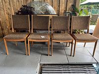 Four teak mid-century chairs with brown woven fabric arranged on a floor, showing front views and side angles.