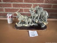 Full view of the vintage resin elephant figurine group with five elephants on a wooden base, next to a can of soda for size comparison.
