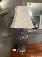 Front view of the vintage mid century modern Asian ceramic table lamp with white shade and glossy gray ceramic body on brass-accented base.
