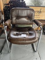 Front view of brown leather vintage cantilever chair with chrome tubular frame, showing seat and backrest tufting and padded armrests.