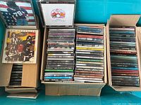 Boxed assortment of CDs featuring visible cases of Led Zeppelin and Queen albums along with various other artists in standard jewel cases and DVD-Audio discs.