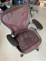 Front three-quarter view showing burgundy mesh seat and back, padded armrests, caster base