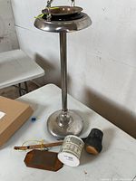 Full view of the metal ashtray on stand, wooden plaque, ceramic cup, carved wooden object, and wooden stick arranged on a table.