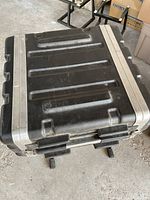 Black hardshell road case closed showing metal reinforced edges and surface indentations.