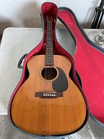 Full view of the acoustic guitar placed inside the open hard case showing wood finish, black pickguard, and some string wear.