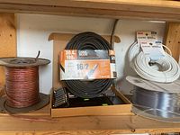 Photo showing an overview of various wires on a shelf including a large copper speaker wire spool, Carol Brand 16/2 gauge power cable in box, RCA CAT5E white network cables, and a clear coaxial cable spool