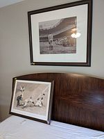Photo showing two framed vintage baseball prints on and above bed headboard, one print leaning and one hanging on the wall.