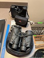 Three pairs of binoculars with cases on a table, with visible straps and carrying pouches.