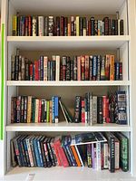 Four shelves of assorted hardcover and paperback books with diverse titles mainly in sports and fiction.