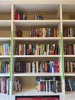 Wide shelf view showing multiple rows of books in various sizes and colors organized on white shelves.