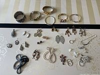 Top-down view of assorted earrings and rings spread out on a white surface, showing a variety of styles and designs including dangles, hoops, and studs.