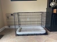 Full view of the black metal wire dog crate with the door open; white cushion inside.