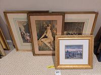 Four framed prints displayed leaning against a wall on carpet. Visible prints include a nude woman painting and two interior scenes.