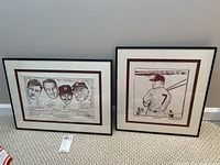 Two framed and matted sports comic prints from Daily News, showing cartoon style baseball themed prints with brown matting and black frames.