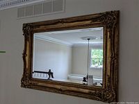 Front view of the large rectangular wall mirror showing beveled glass and ornate gilded frame with floral and scroll design details.