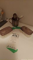 Photo showing two sterling brushes, sterling cup containing spoons and toothbrush, MaxSold tag with lot details.