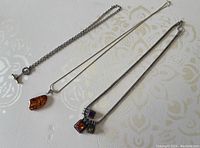 Three sterling silver necklaces side by side including amber pendant and marcasite charm necklace