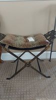 Full view of metal vanity stool with leopard print cushion on a carpeted floor against an off-white wall.