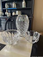 Three crystal items on table: Waterford vase at center back with diamond cut, and two Orrefors crystal bowls in front - one larger fluted scalloped, one smaller ribbed.
