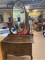 Front view of antique wooden dresser with attached oval swivel mirror showing tiger stripe wood grain and metal ring drawer pulls.