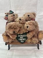Front view of five plush bears sitting on a wooden bench holding a chalkboard sign 'Families are Forever'.