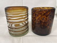 Photo showing two hand blown glass items side by side. One clear with amber spirals, the other amber with mottled spots.