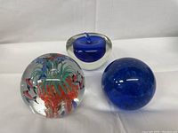 Three glass paperweights on white background. One fish and coral scene, one blue apple shape, one solid blue sphere.