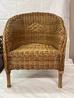 Front view of child's wicker chair showing woven seat, curved armrests, and woven back with diamond pattern detail.