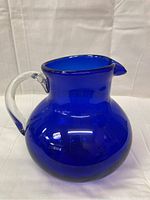 Full view of cobalt blue rounded glass pitcher with clear handle, showing bulbous shape and pouring spout.