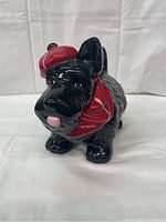 Front view of the black Scottish Terrier dog biscuit jar with red hat and scarf showing facial features and front feet.