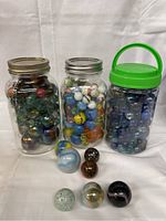 Three jars of marbles and seven loose marbles arranged in front of the jars on a cloth background.
