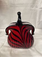 Front view of Murano glass purse vase showing red and black swirl design and curved handle.