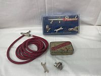 Full setting of Paasche airbrush kit including hose, airbrush gun in plastic case, small wrench, mounting bracket, and vintage tin container.